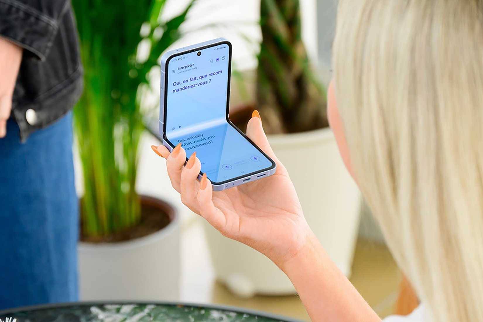 Một người phụ nữ cầm điện thoại Samsung Galaxy Z Flip 7 sử dụng ứng dụng Interpreter